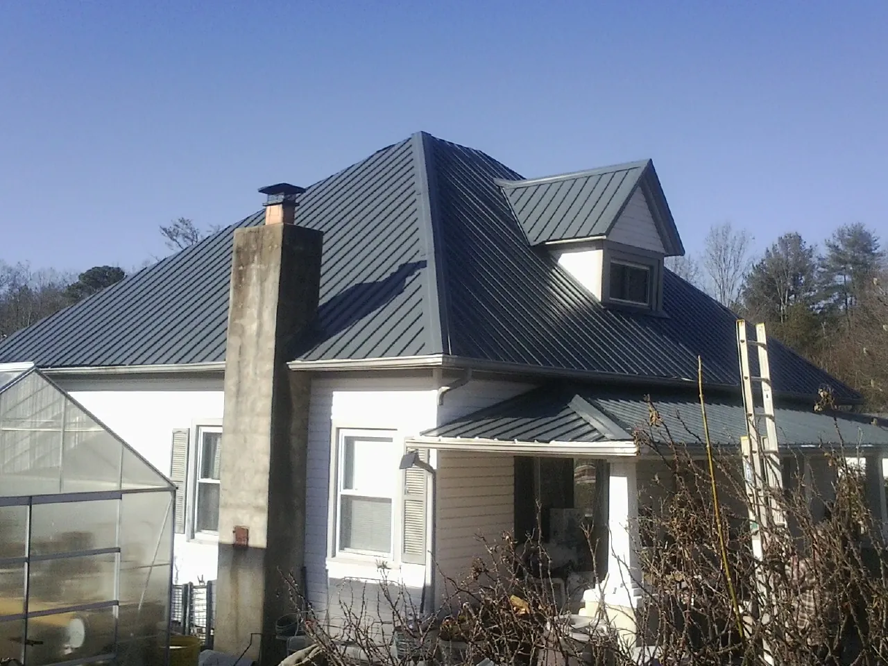 Dark blue standing seam metal roof on a white farmhouse with dormer — Slate & Tile Roof Repair by Roofing Brothers in Mc Grady