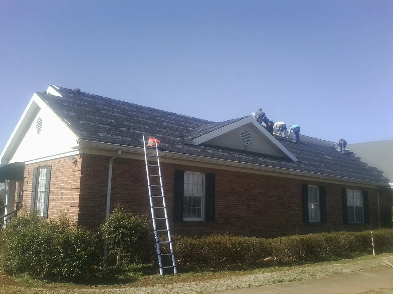 Crew tearing shingles off a brick ranch roof with a ladder set — Emergency Roof Repair work by our crew in Mc Grady