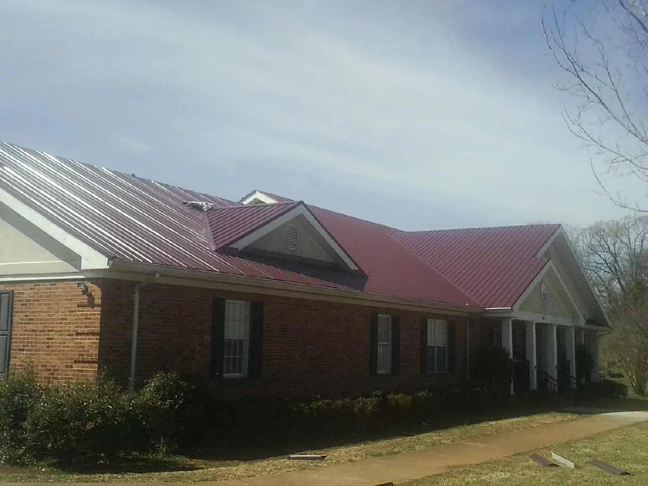 Red metal roof with gabled entries on a long brick building, from a Hail Damage Roof Repair job in Mc Grady