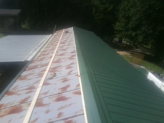 Old rusted panels beside newly installed green metal roofing — Wind Damage Roof Repair by Roofing Brothers in Mc Grady
