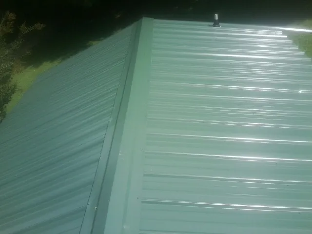 New green metal panels meeting at the ridge of a roof — Flat Roof Repair work by our crew in Mc Grady