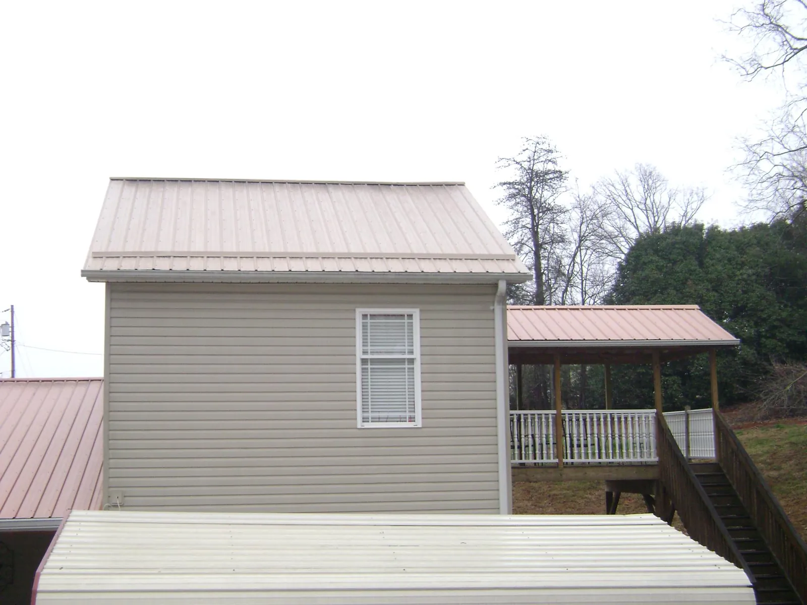 Tan metal roofs on a two story addition and attached porch, from a Roof Replacement job in Mc Grady